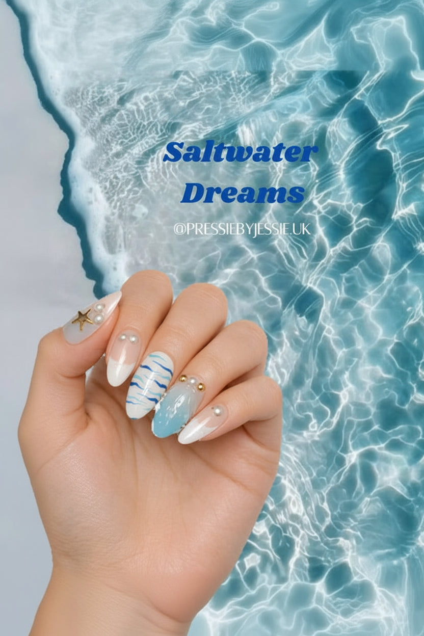 A hand with decorative white, light blue, and gold nail art is shown against a background of rippling ocean water. The text 'Saltwater Dreams' and '@PRESSBYJESSIE_UK' are overlaid on the water.